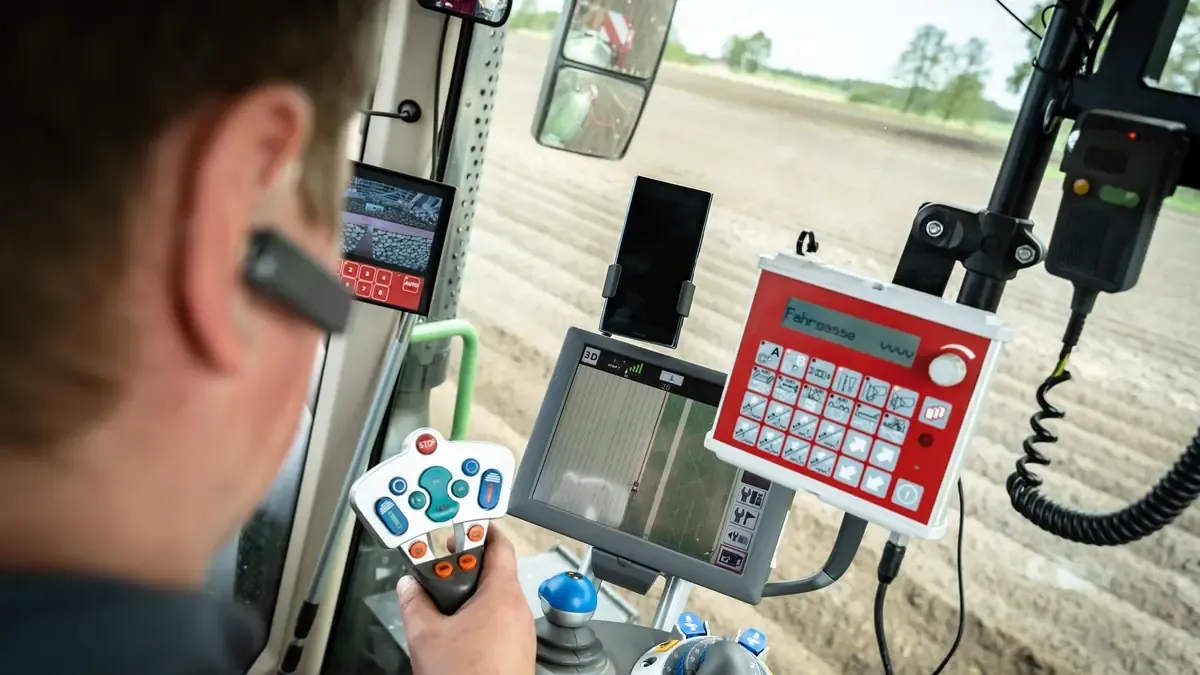 Vue par-dessus l'épaule d'un conducteur dans une cabine de tracteur, entouré d'écrans et de consoles de guidage